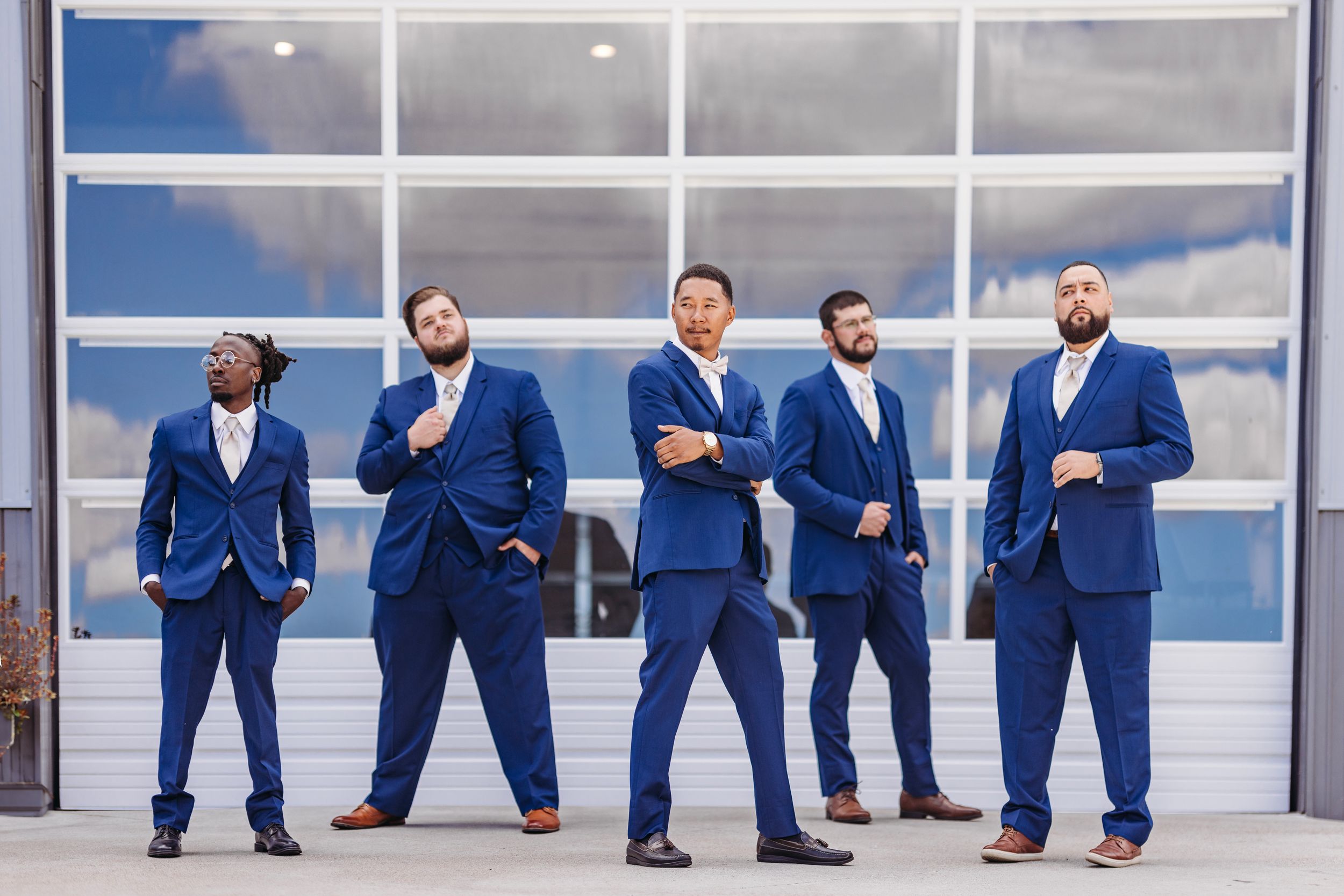 Groomsmen in matching navy blue suits strike playful poses in a modern architectural setting.Middle TN wedding photographer