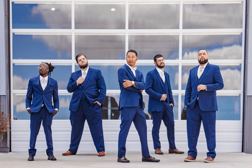 Groomsmen in matching navy blue suits strike playful poses in a modern architectural setting.Middle TN wedding photographer