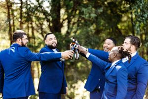 Wedding party in blue suits raises champagne glasses for a celebratory toast in an outdoor setting. Middle TN wedding photographer