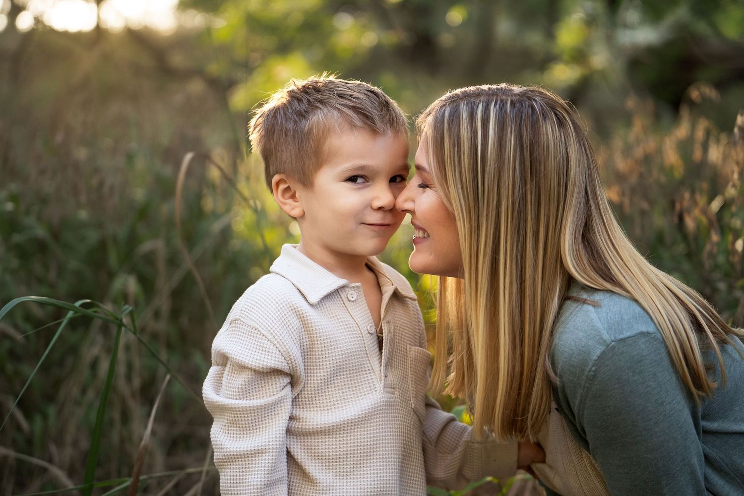 a mother in a green sweater touches are son's nose with her own