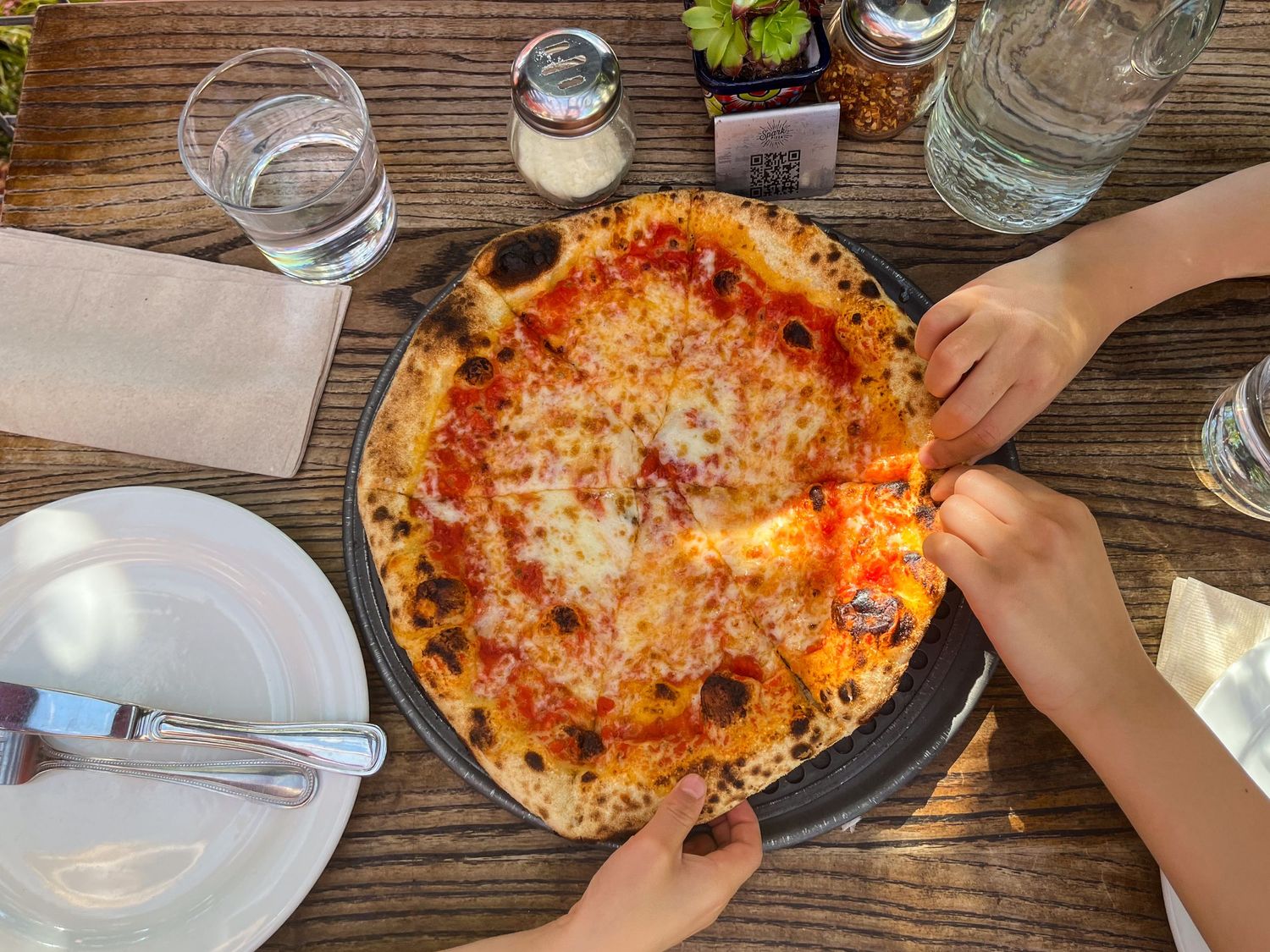 Children's hands grabbing cheese pizza slices at Spark Pizza.