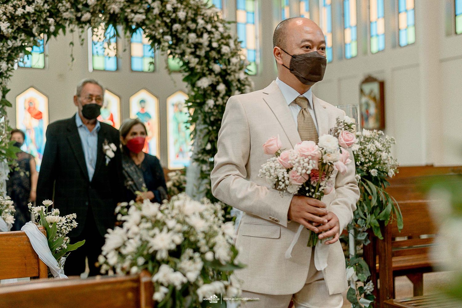 Wedding ceremony in church with elegant floral arch and light grey suit.