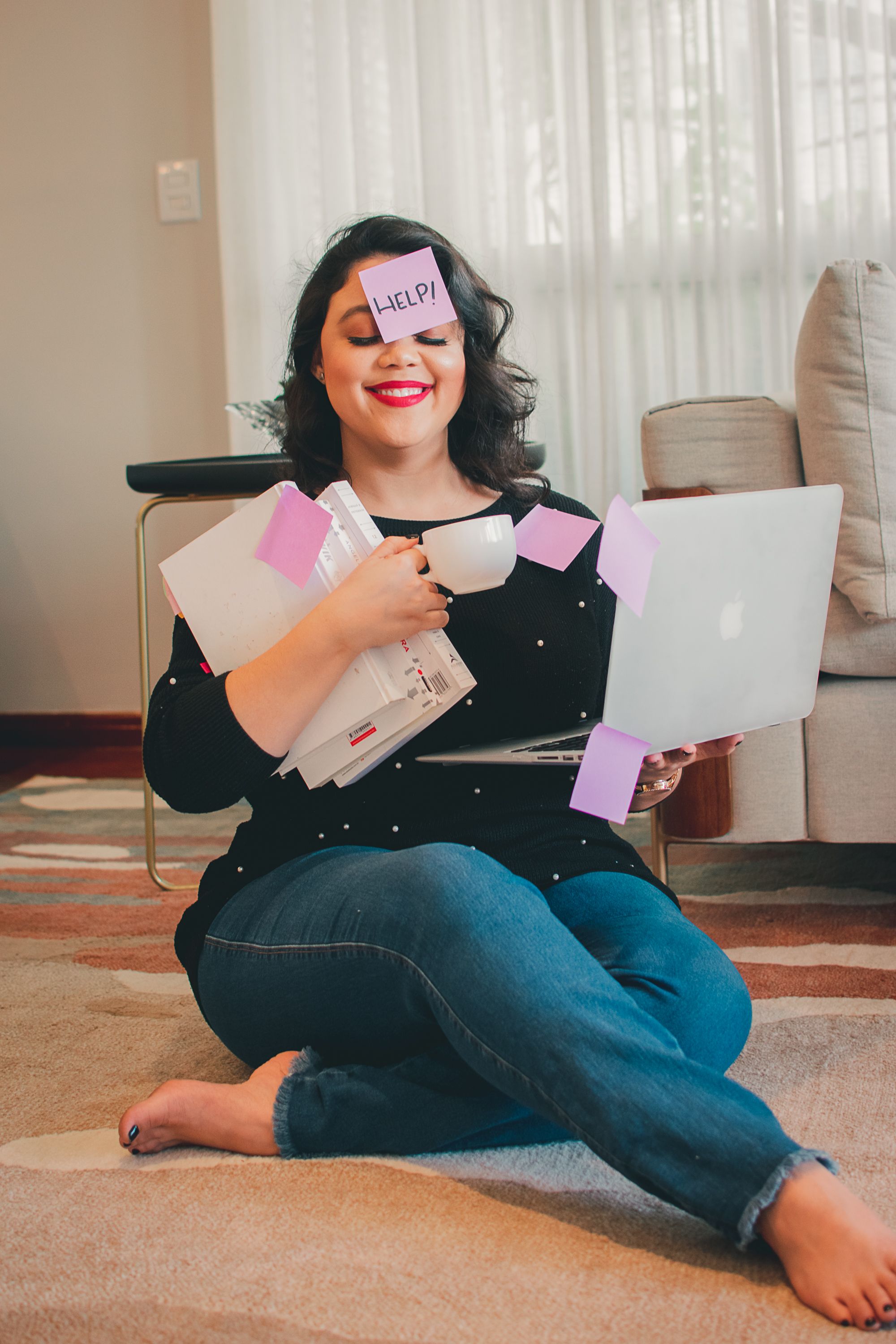 Someone surrounded by sticky notes works on laptop while sitting on floor.
