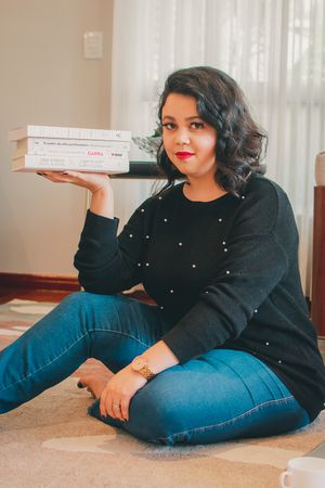 Someone in black sweater and jeans balances stack of delivery boxes while sitting on floor.