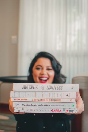 Stack of books photographed with a bright smile and joyful expression against a light background.
