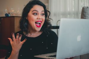 Excited person gesturing with hand while looking at laptop screen with enthusiastic expression.