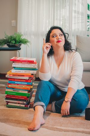 Person sitting casually next to stack of colorful books while talking on phone in home environment.
