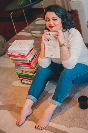 Person relaxing on carpet with collection of books while reading in comfortable home setting.