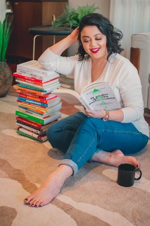 Reader enjoying book while sitting on floor next to tall stack of colorful literature.
