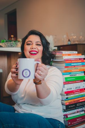 Happy reader holding coffee mug next to impressive stack of books in home setting.