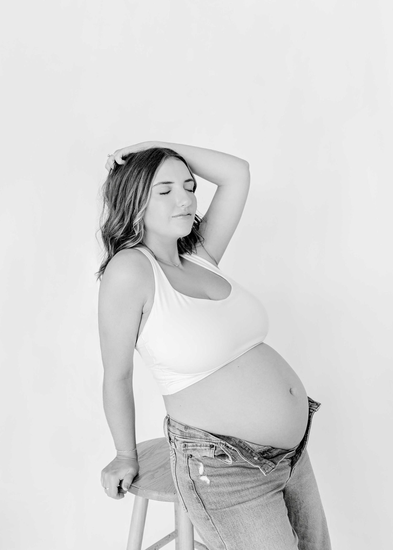 Black and white maternity portrait showing artistic pose against white background.