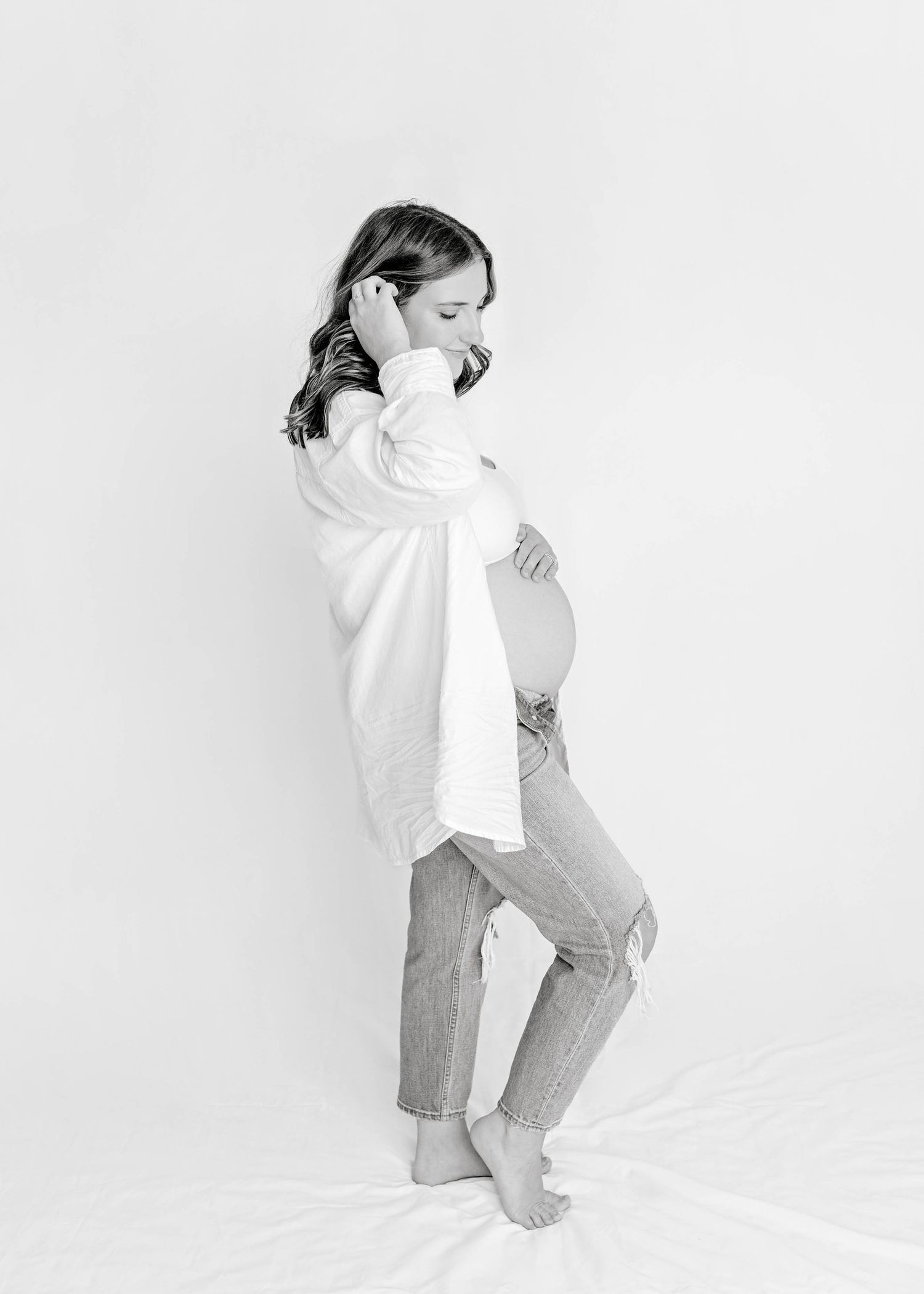 Black and white maternity portrait in relaxed pose with white shirt and jeans.