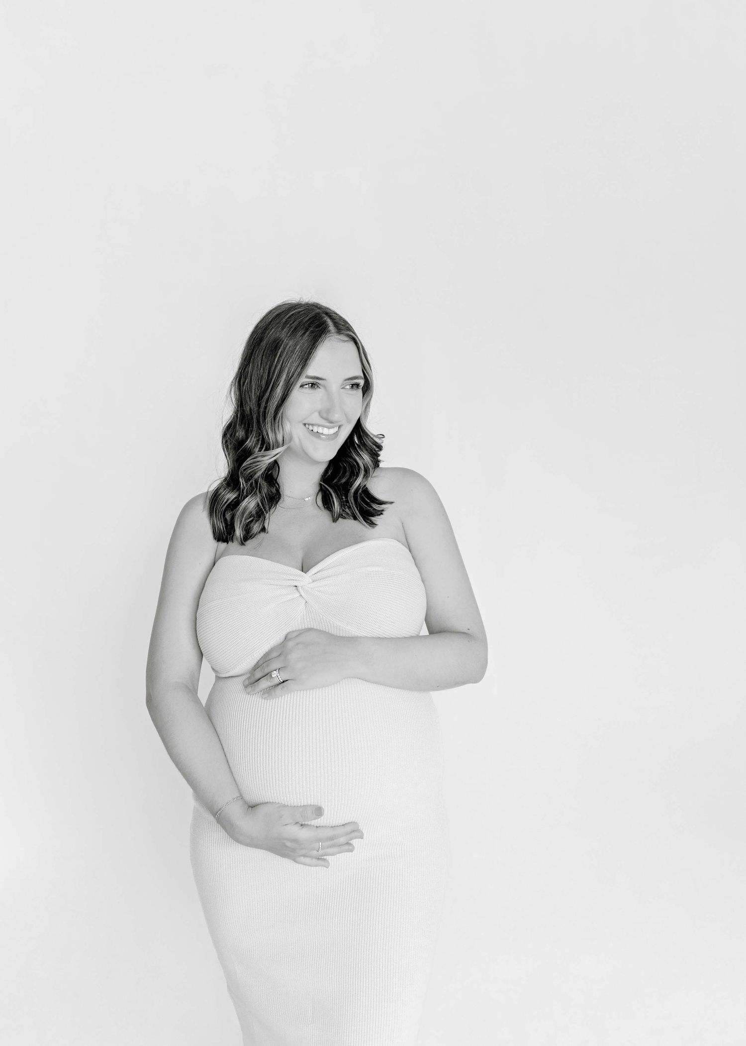 Black and white maternity portrait against white background showing gentle curves in fitted dress.