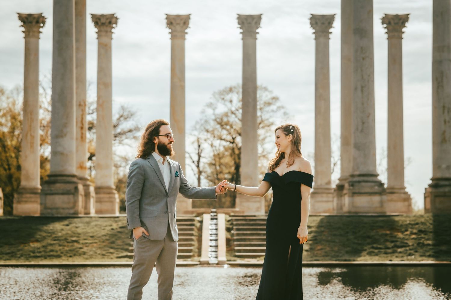 Romantic couple poses among classical stone columns at sunset.