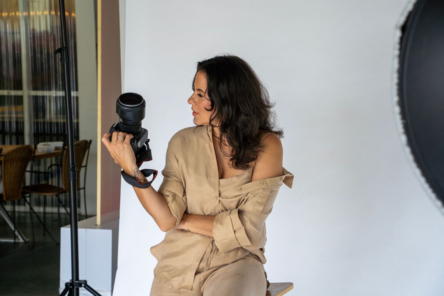 A photographer holding a camera in a beige suit in a studio setting.