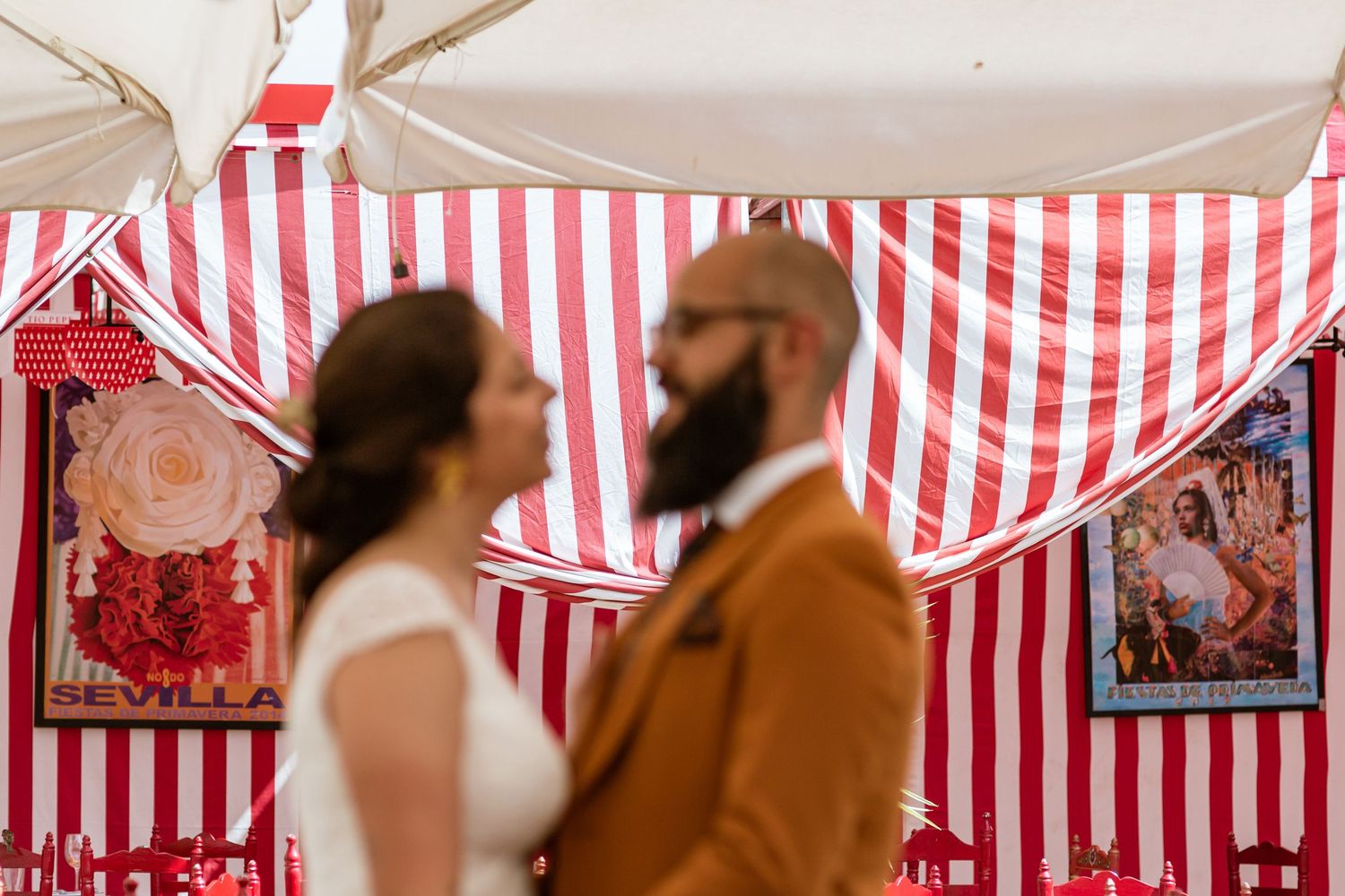 Wedding couple stands under red and white striped tent canopy with decorative posters on display in Seville, Spain