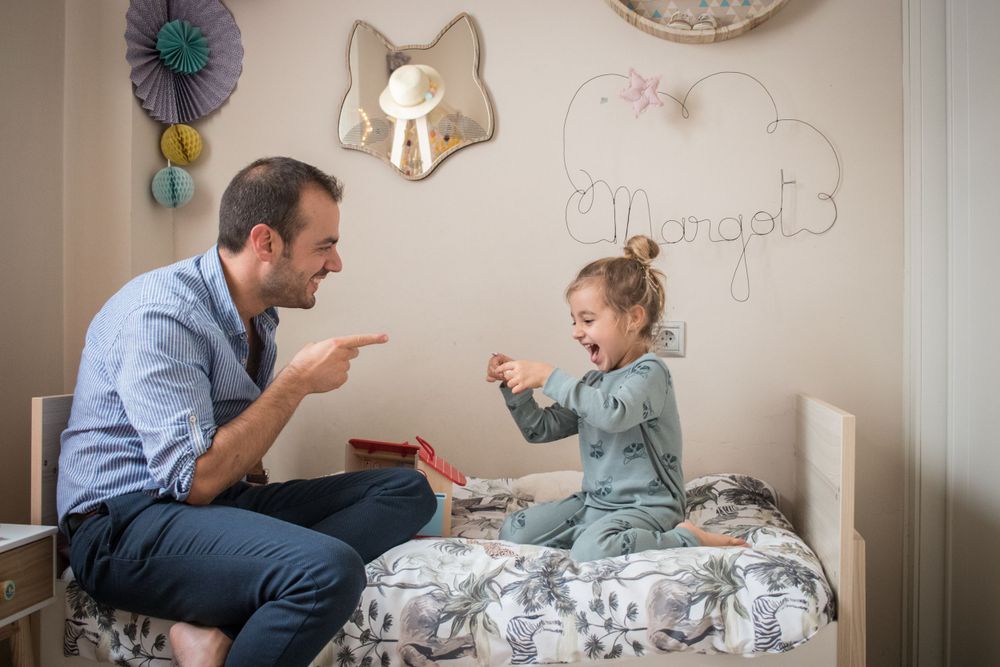 Playful interaction between parent and child on a decorated bedroom bed.