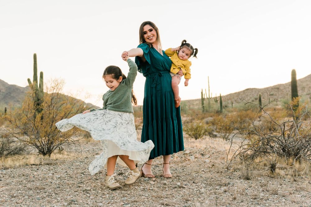 Desert family scene with emerald dress against mountain landscape with saguaro cacti.