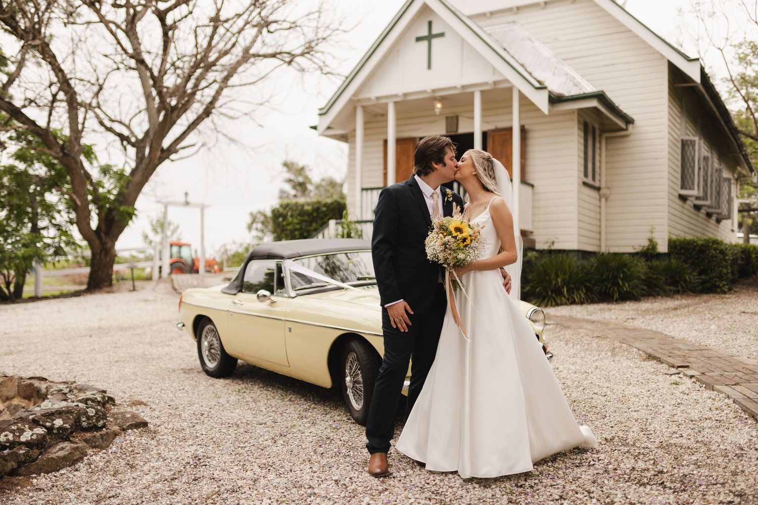 Bride & Groom kissing in front of vintage Car and Church