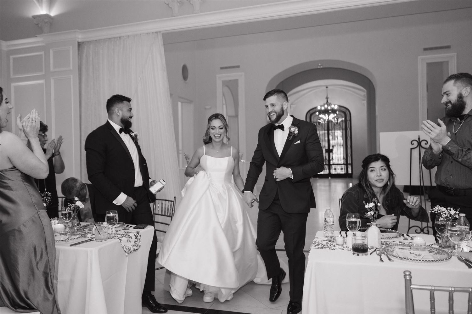 Wedding reception moment in an elegant white ballroom with guests at dining tables.