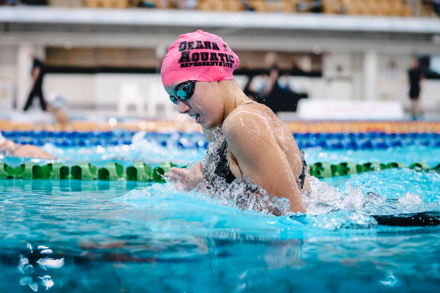 Swimmer in pink cap performing breaststroke during competitive race.