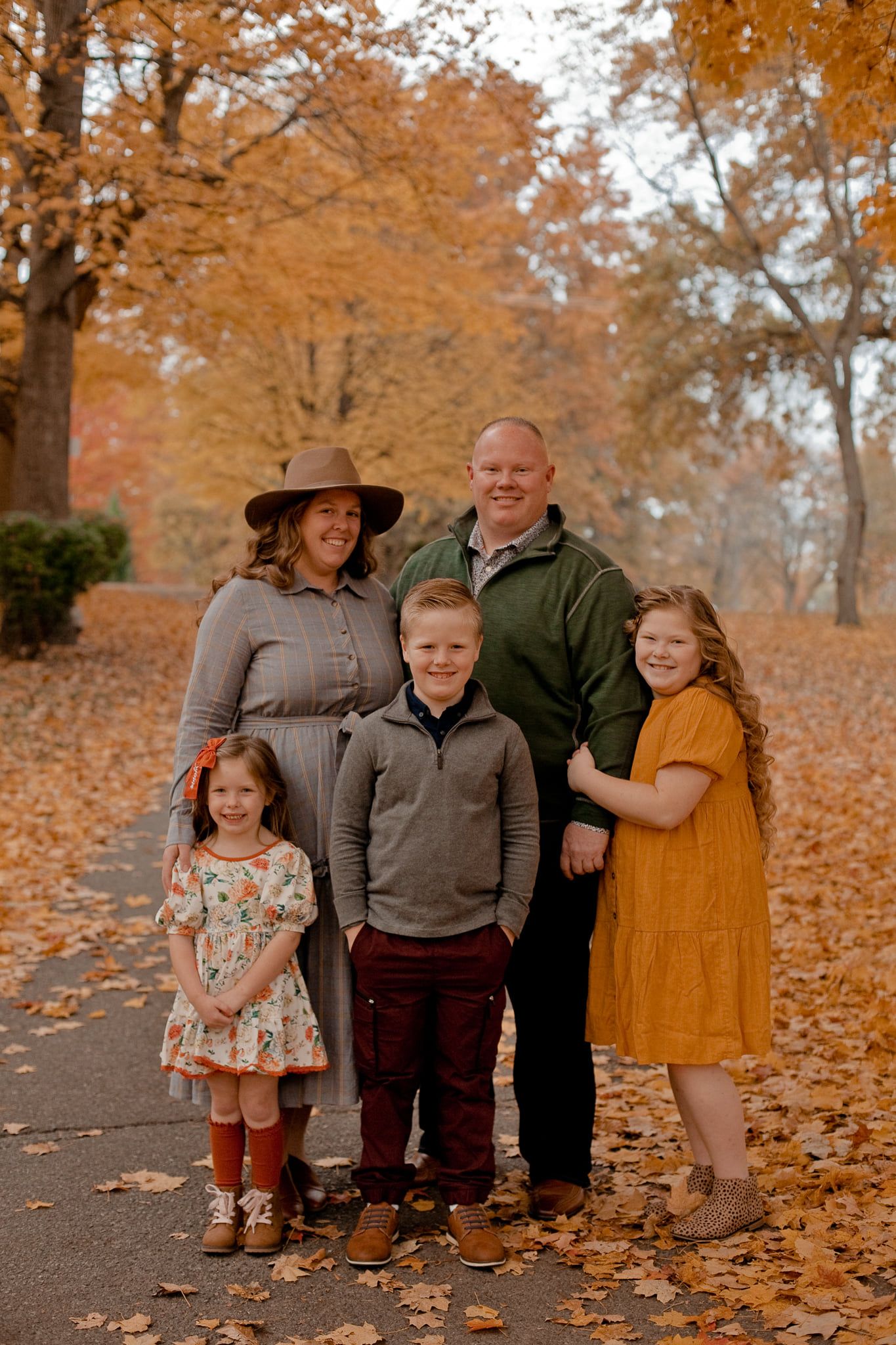 Family group poses together on fallen autumn leaves during an outdoor photo session.