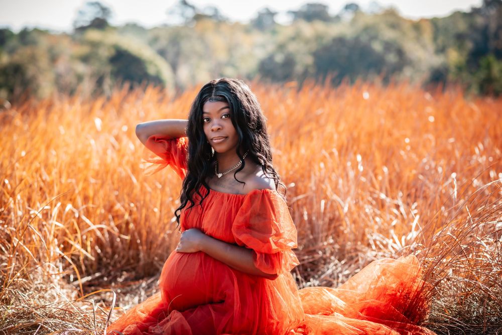 Glowing maternity portrait in bright orange dress surrounded by golden grass.
