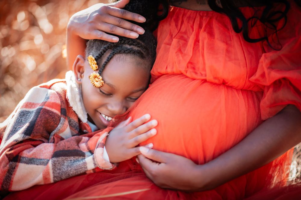 Sweet moment captured between child and expectant mother in bright orange dress.