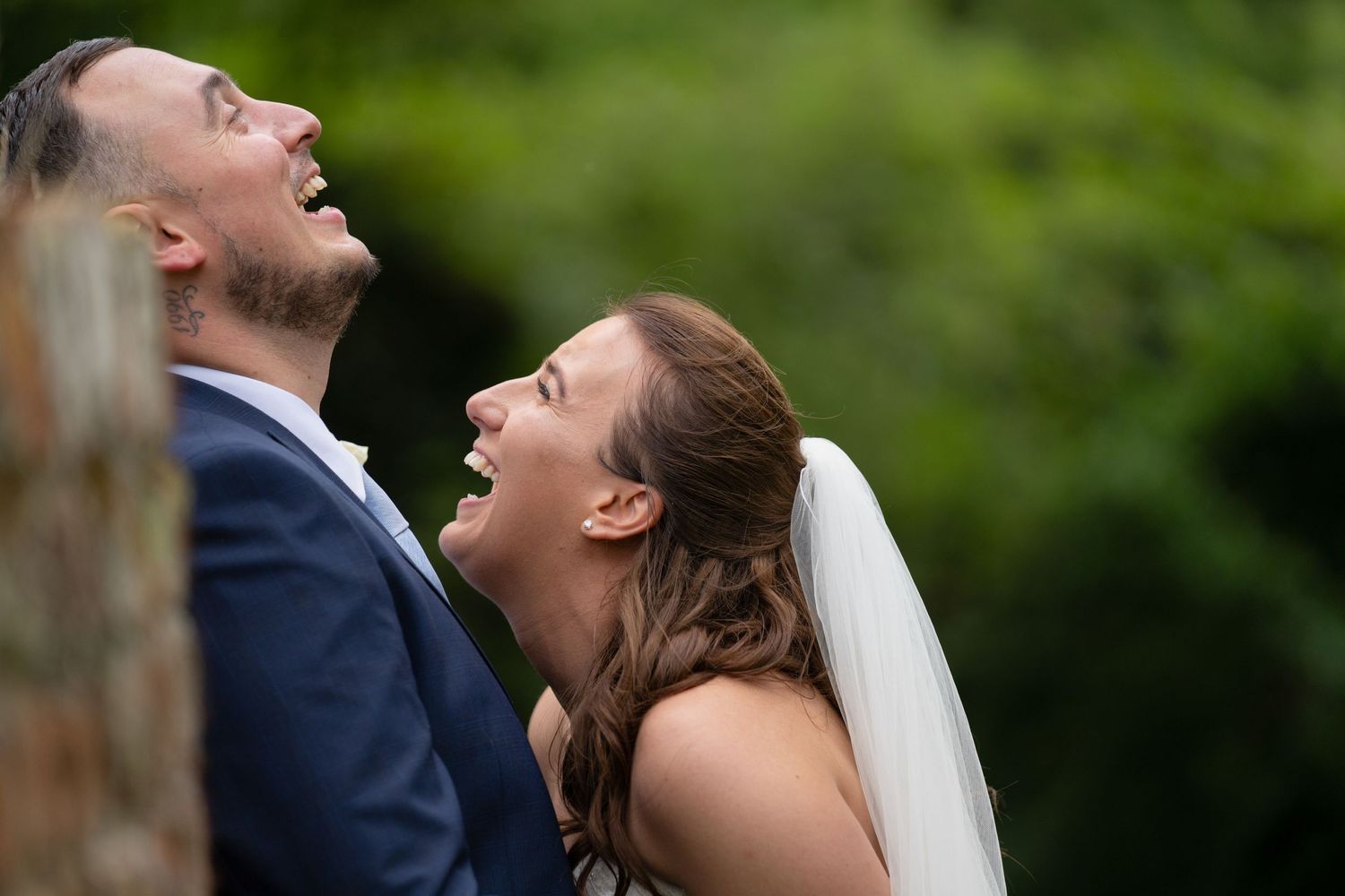 Joyful wedding couple laughing together outdoors in natural lighting.