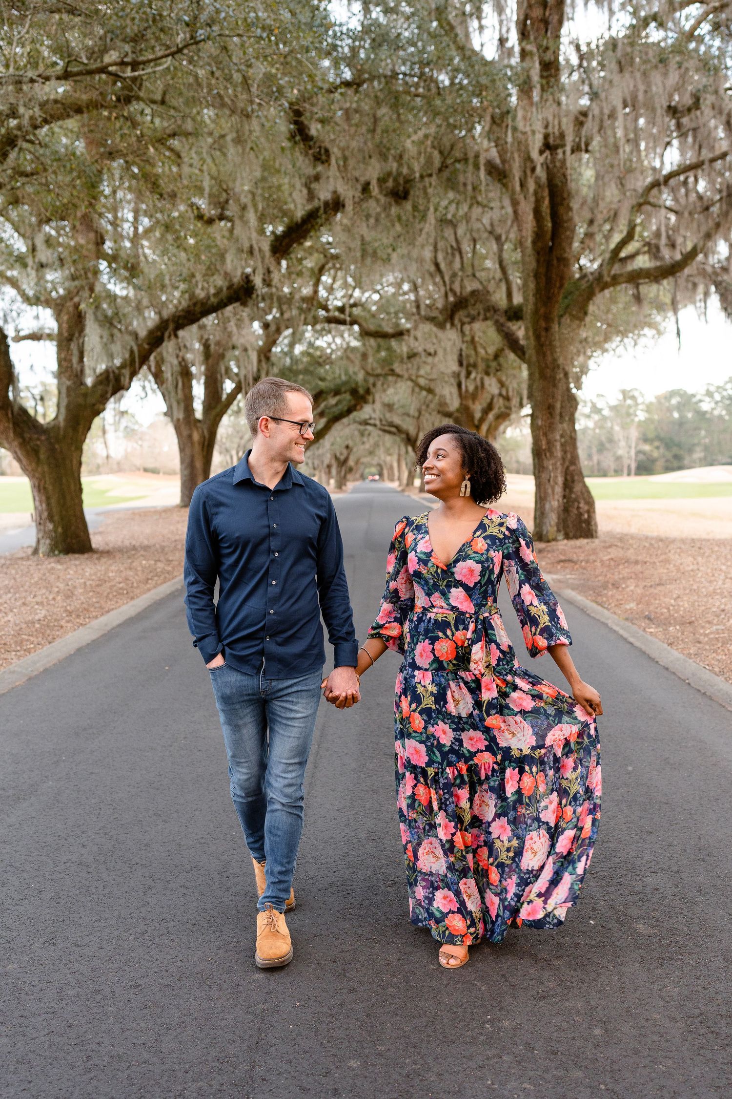 Couple walking together on a tree-lined path with Spanish moss hanging from oak branches.
