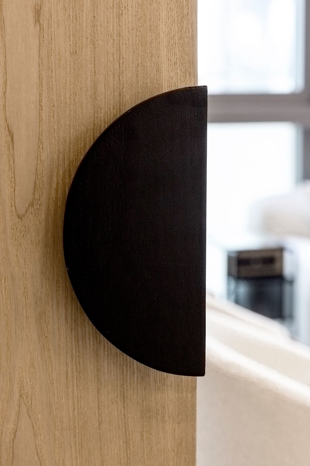 A black semicircle door stop mounted on a light wooden wall.