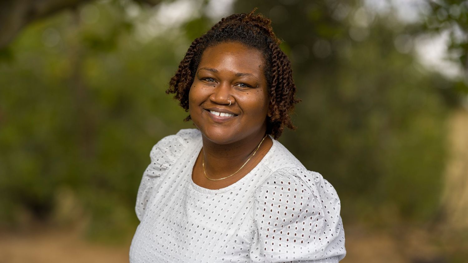 Headshot of an black woman in a white t shirt outside