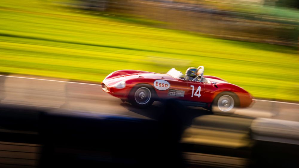 Vintage racing cars competing at high speed on a sunlit racetrack with yellow background.