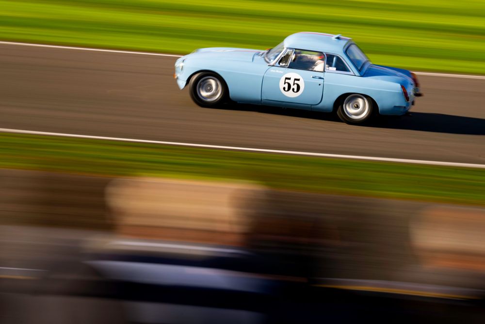 Vintage racing cars speeding along a racetrack with motion blur against vibrant green grass.