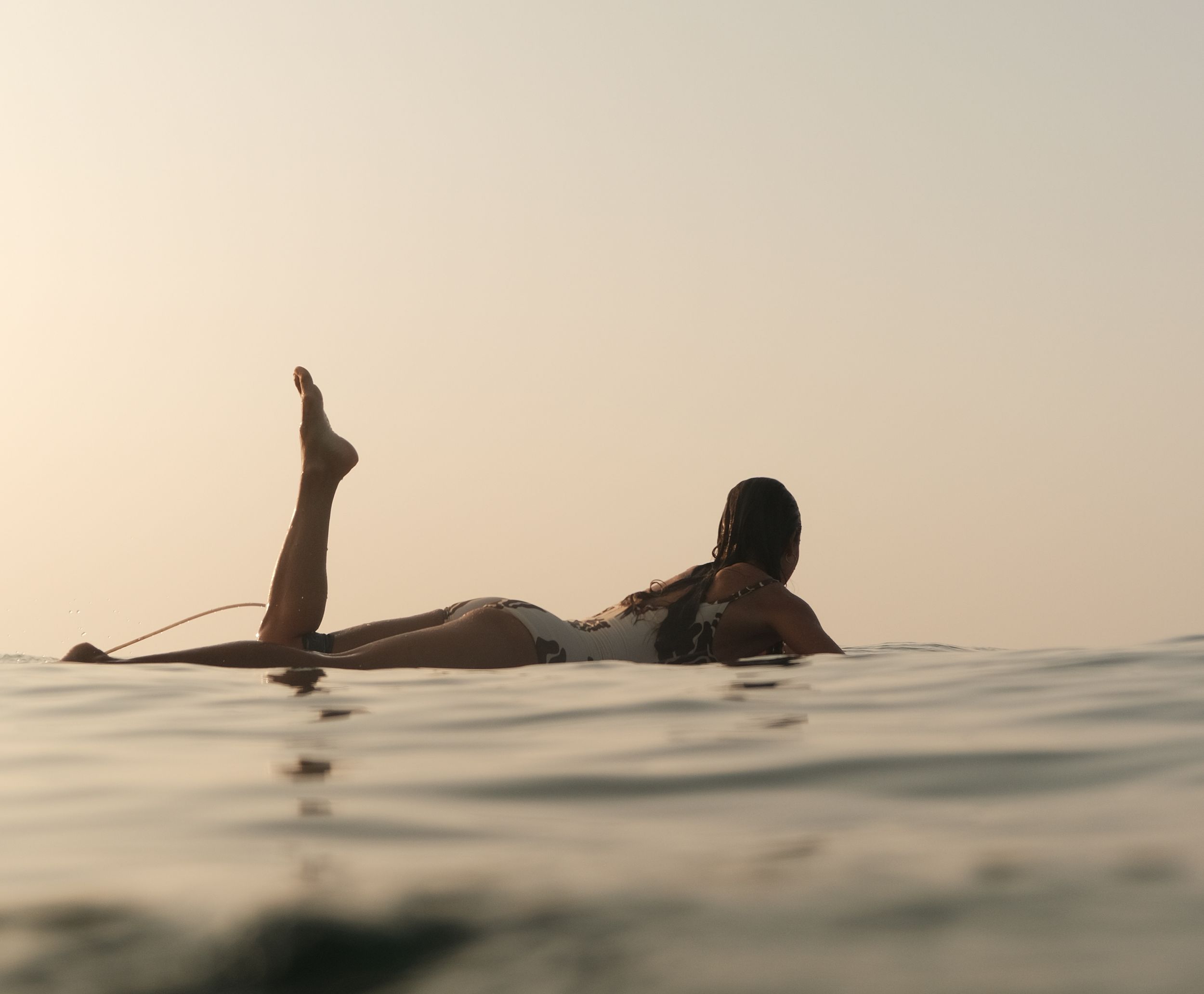 Girl laying on surfboard in water sunrise