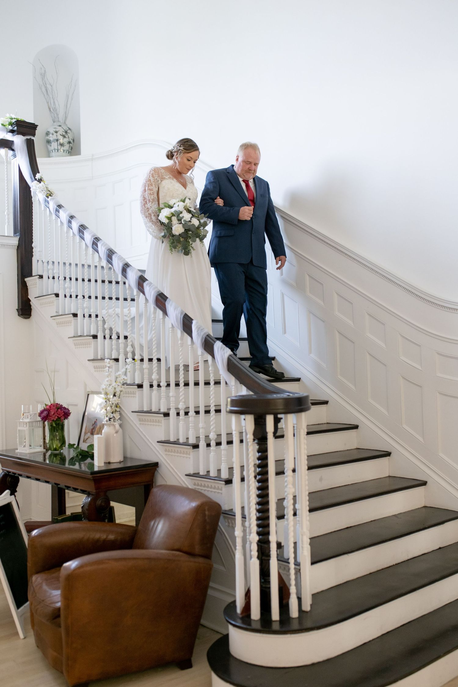 Elegant white staircase with dark wood treads and leather armchair at the landing.