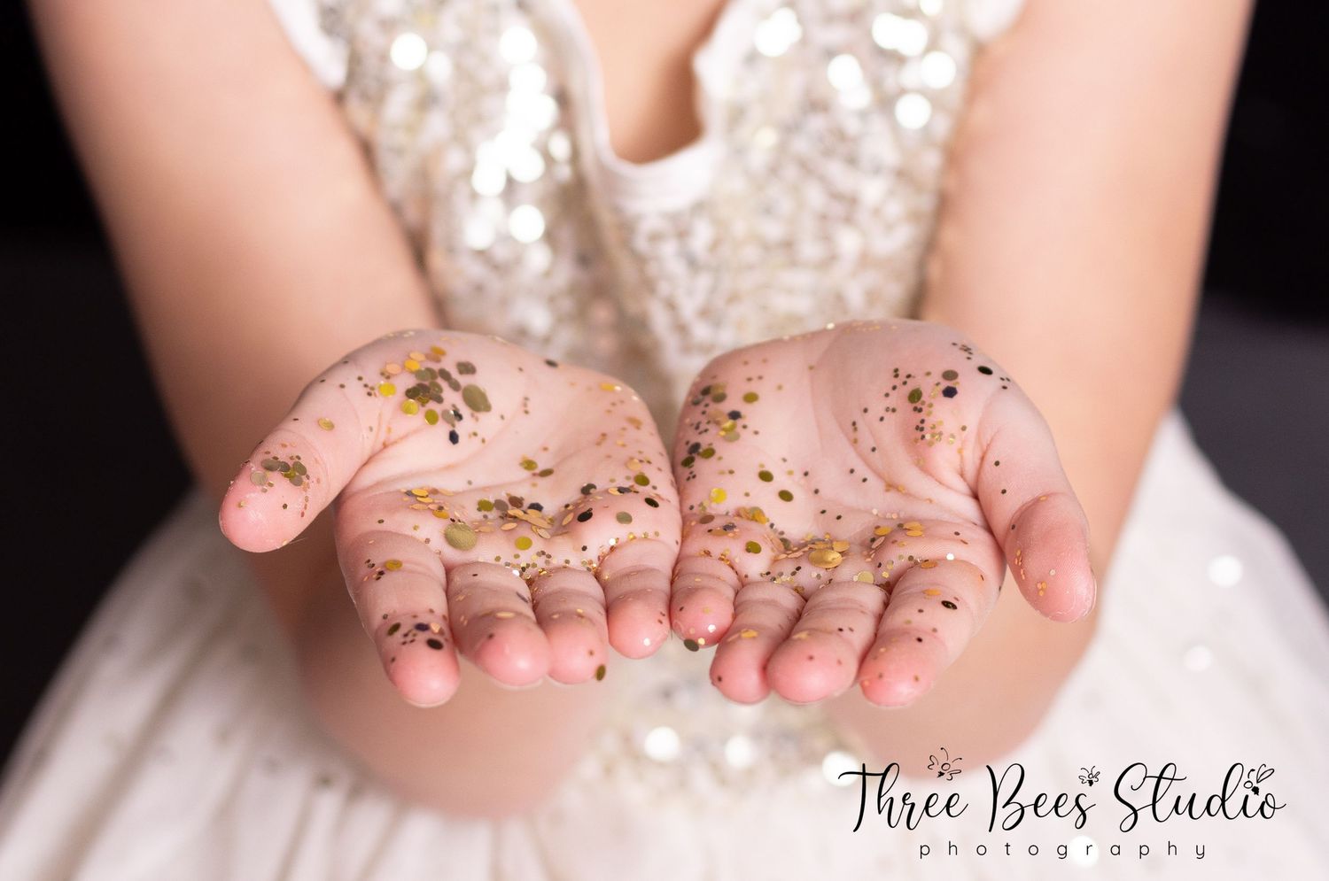 Hands holding sparkling gold glitter in dreamy princess photoshoot.