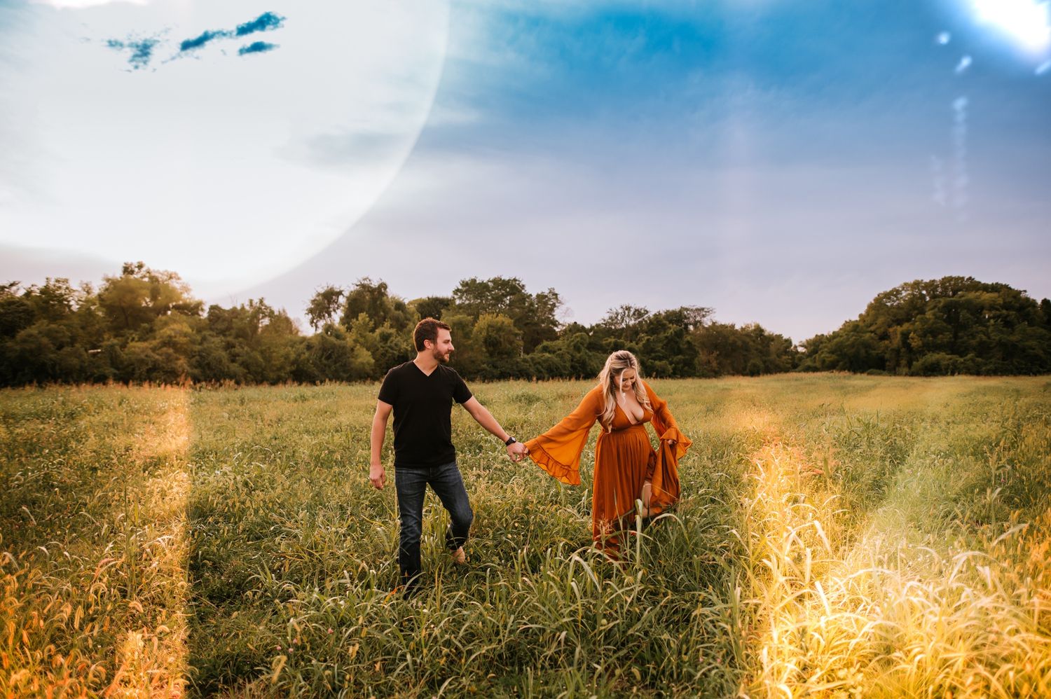 Couple holding hands while walking through a golden sunlit field at sunset.
