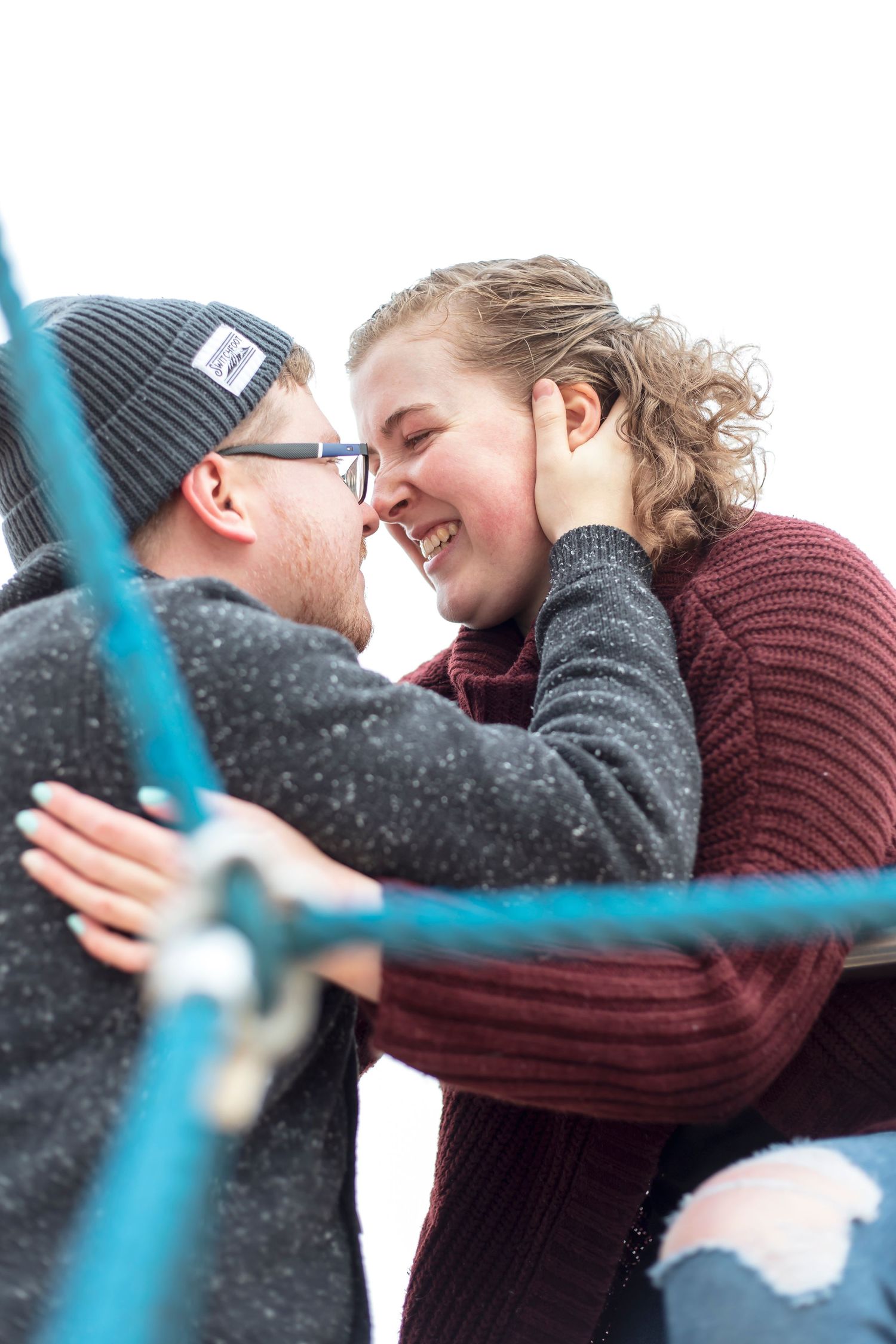 A photograph of a male and female couple looking into deeply each others eyes on a blue rope play structure in Oshawa