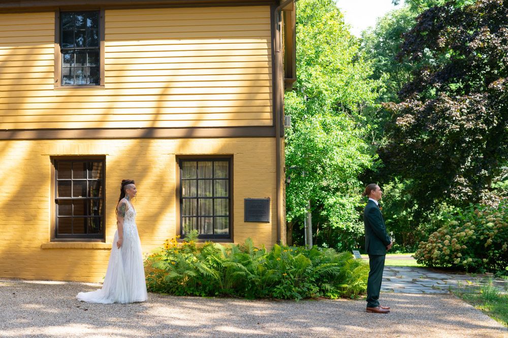 Elegant wedding first look scene against yellow historic house exterior with lush greenery.