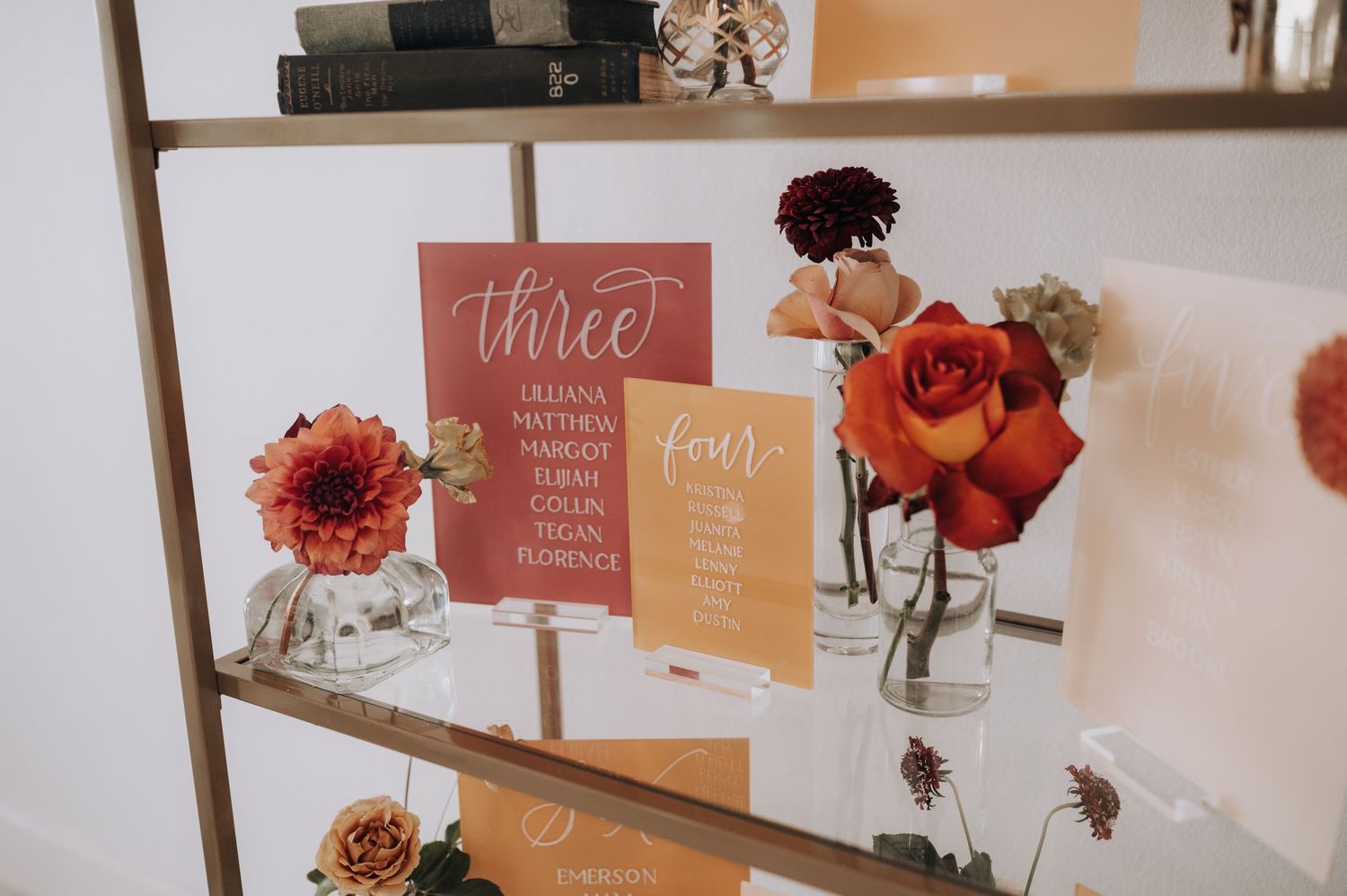 Wedding signage display with coral roses and peach-colored table numbers in modern calligraphy.