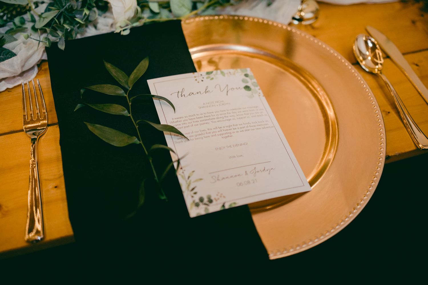 Wedding menu card with greenery on gold charger plate with formal place setting.