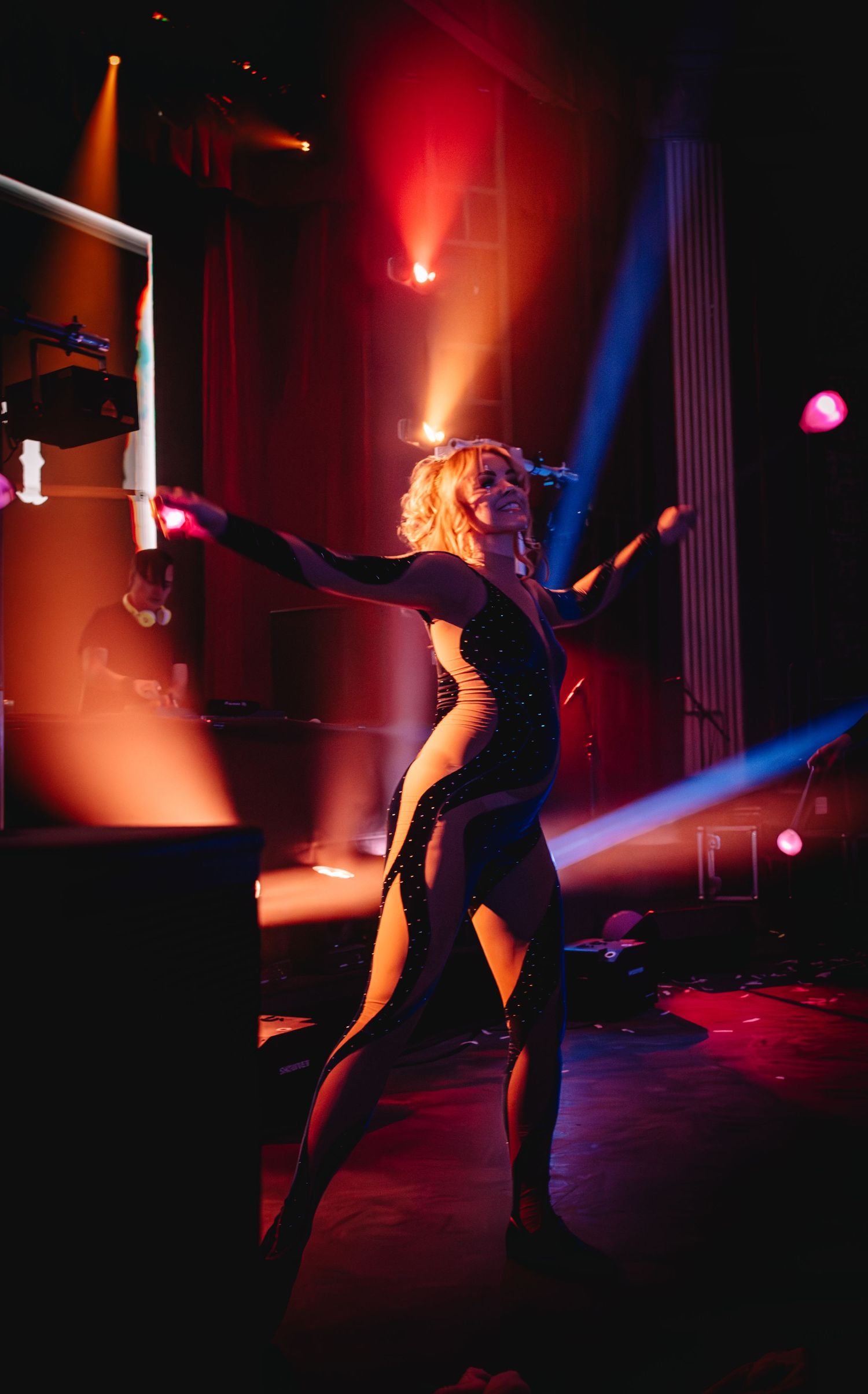 Dancer in black attire performing under dramatic red and blue stage lighting.