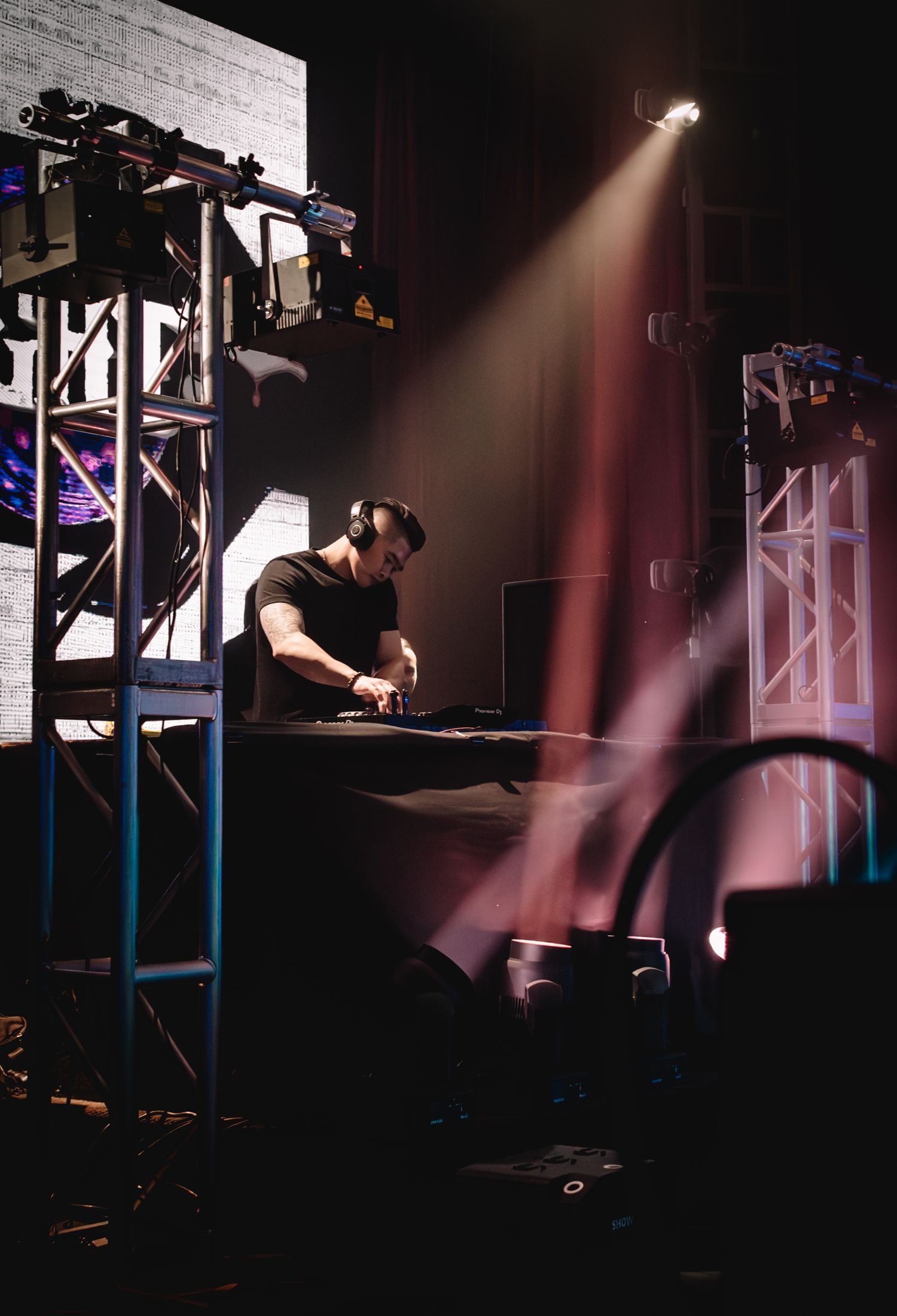 DJ performing at mixing console under dramatic spotlight in dark venue setting.