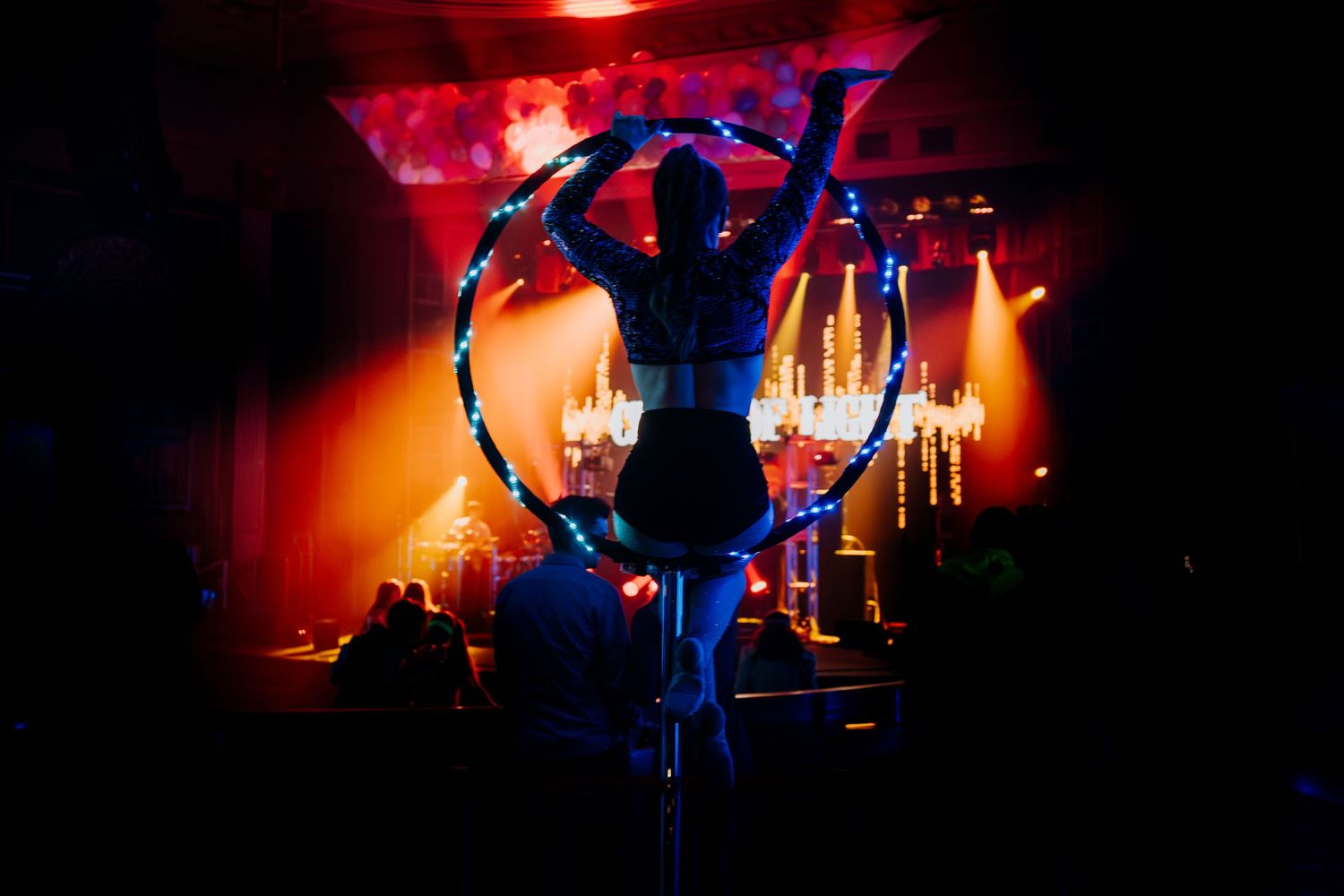 Aerial performer in a luminous hoop against red stage lighting creates dramatic silhouette.