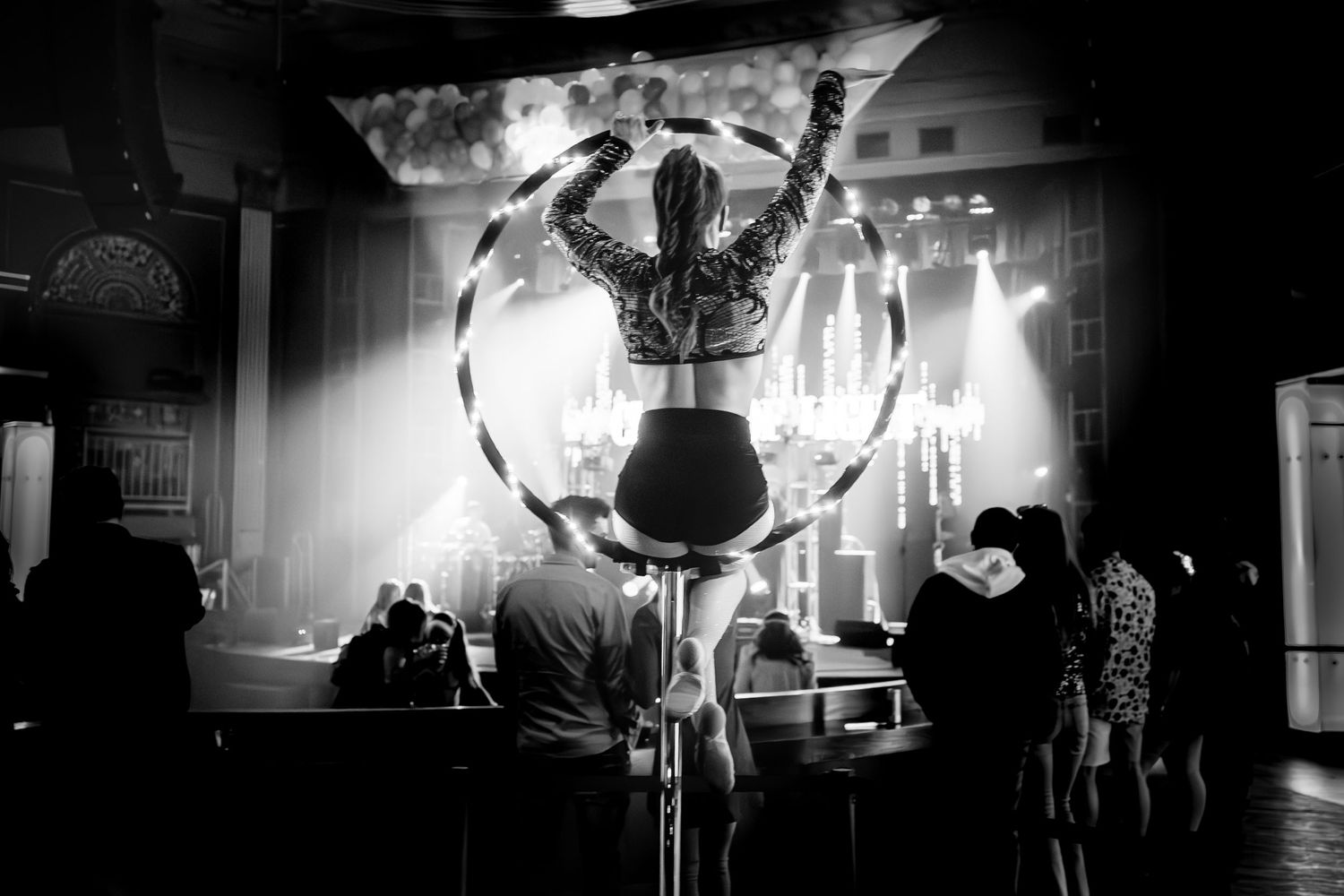 Black and white photo of an aerial hoop performance with audience silhouettes.