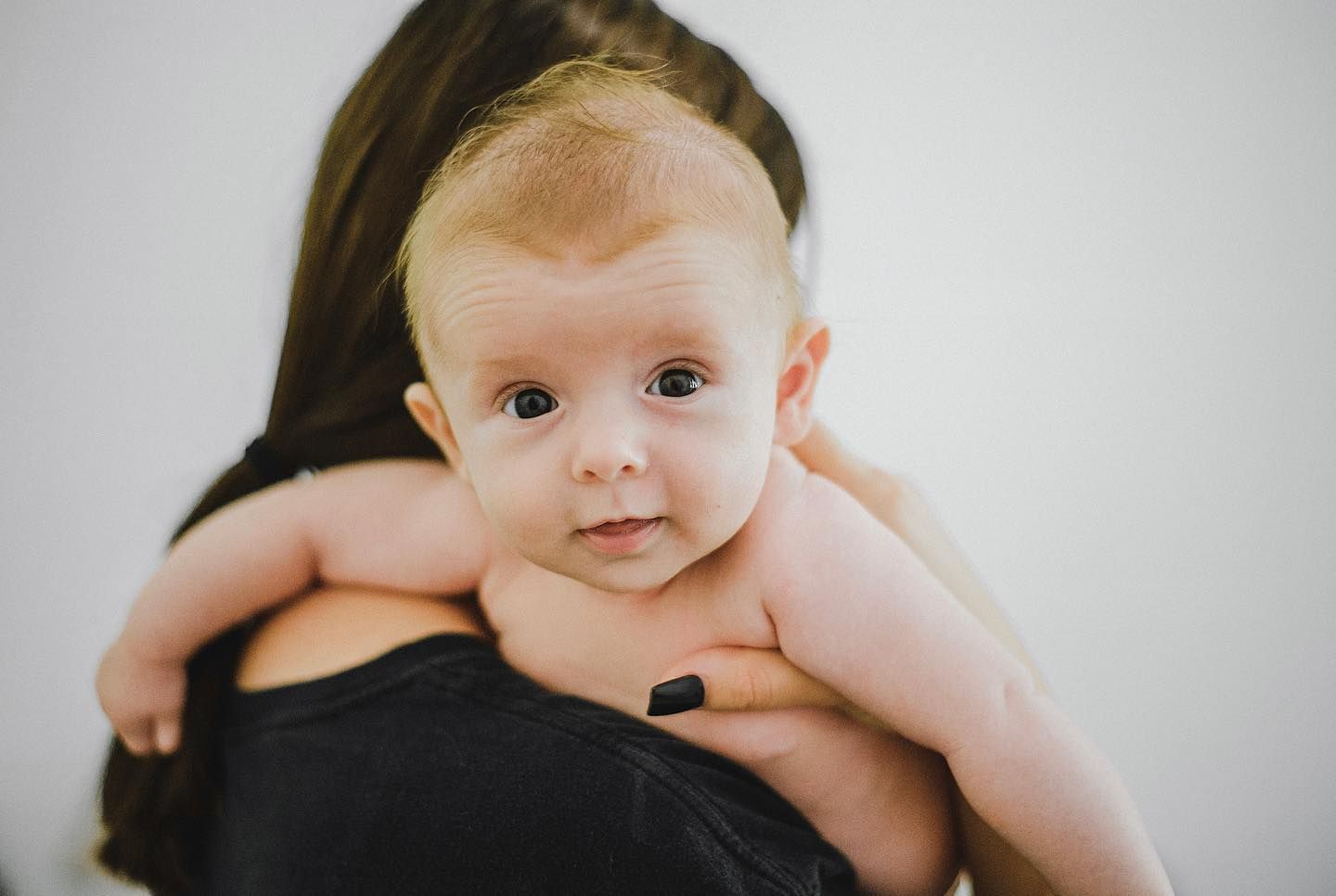 An infant rests gently against someone wearing black in an intimate portrait.