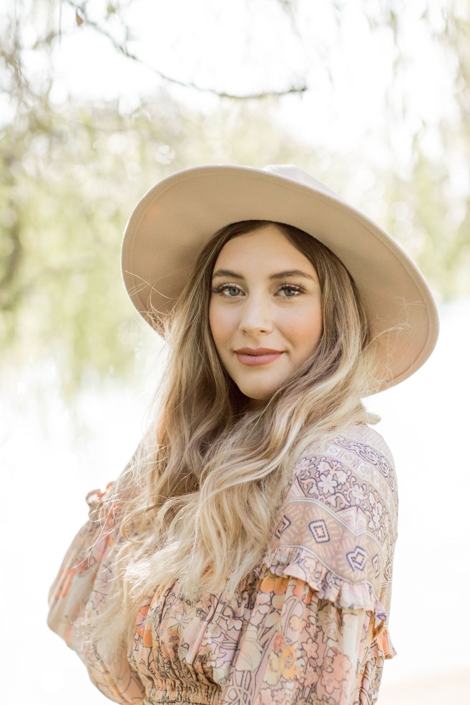 Young blonde woman in floral boho dress wearing a wide-brim tan hat outdoors.