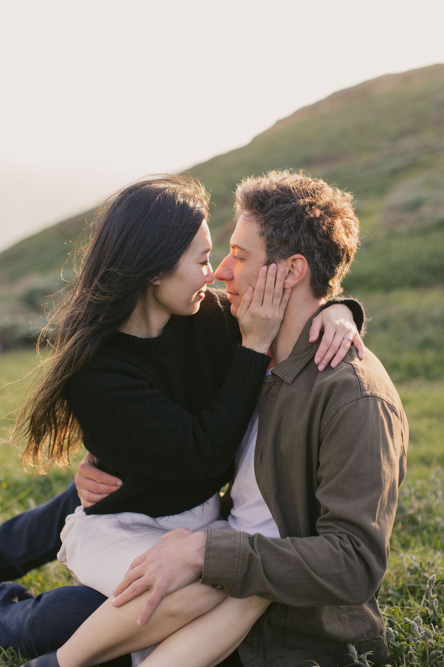 Romantic embrace on a sunlit hillside with ocean views in the background.