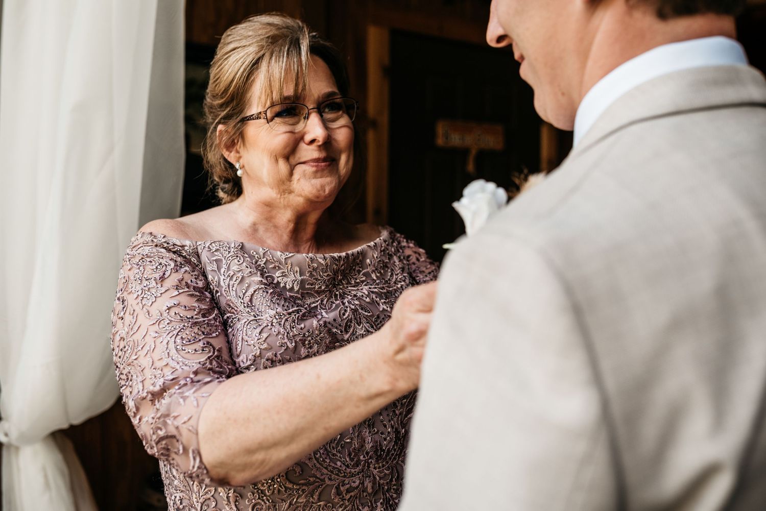 Intimate pre-wedding moment of boutonniere pinning in formal attire.